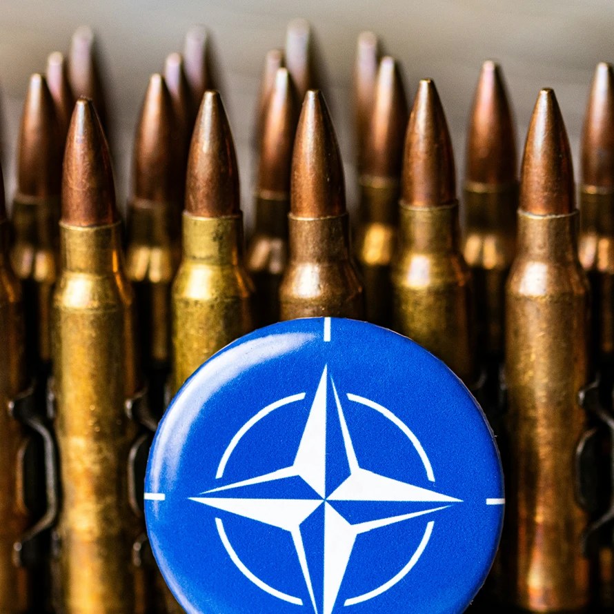 Ammunisjon på rad og rekke foran et lite blått skilt med Nato sitt logosymbol.
